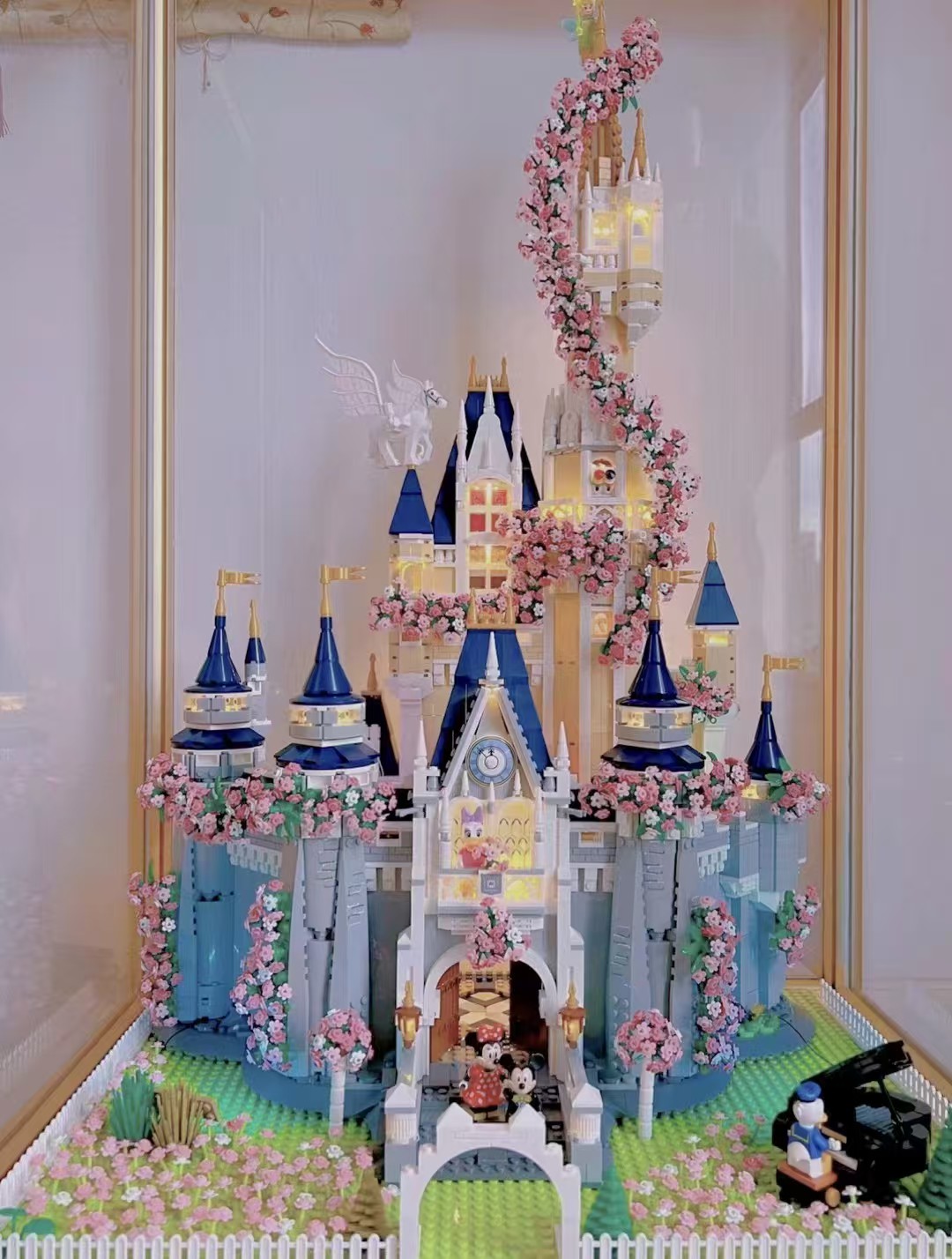 A detailed LEGO castle with pink flowers displayed in a cabinet